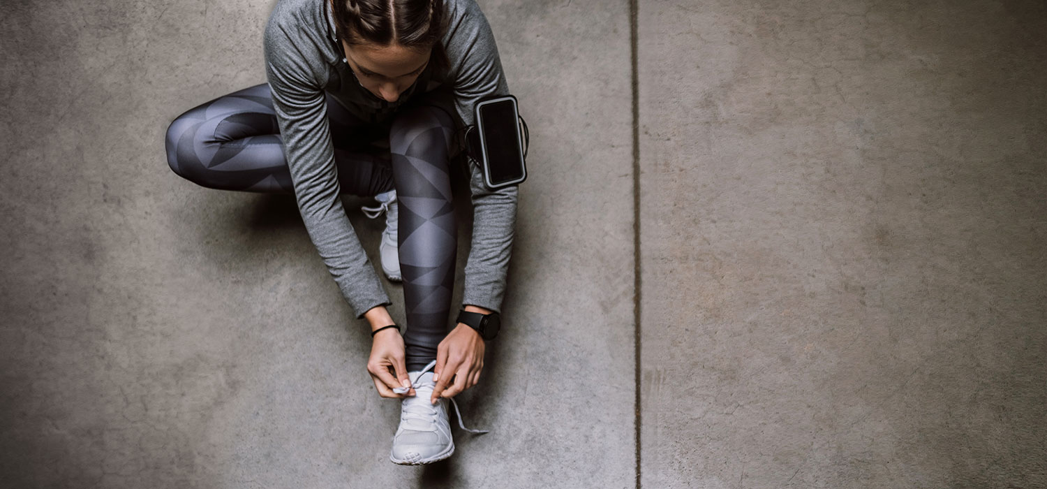Hoe kies je de juiste technische sportkleding? Vrouw in sportkleding die haar sportschoenen vastmaakt
