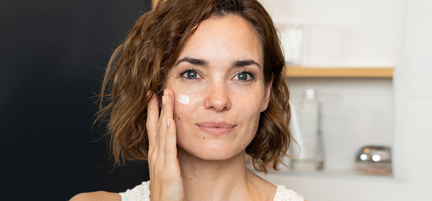 Gids : het kiezen van anti-verouderingsproducten in parfarmacie Vrouw brengt antiverouderingscrème aan op haar gezicht