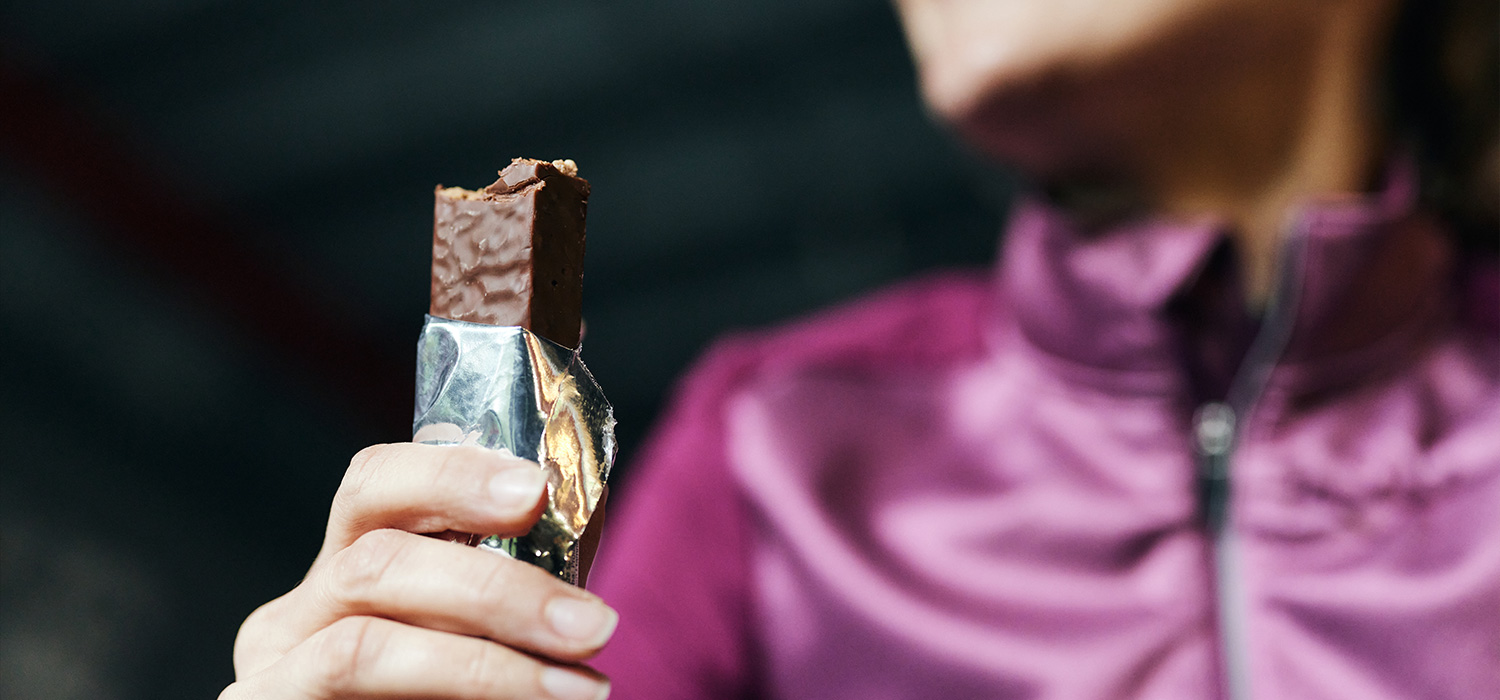 De essentiële rol van eiwitten in sportvoeding Vrouw eet een eiwitreep na het sporten