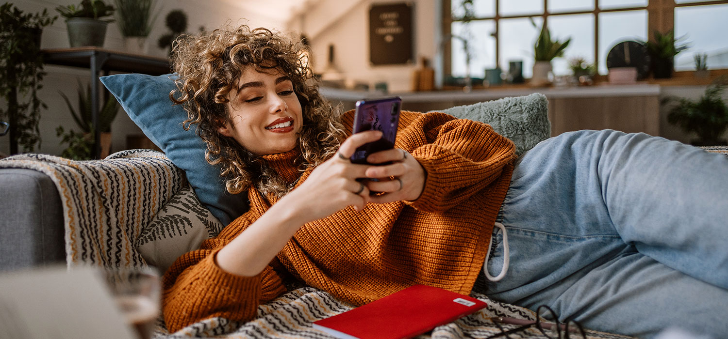 De voordelen van online salonafspraken Glimlachende vrouw met haar telefoon op de bank