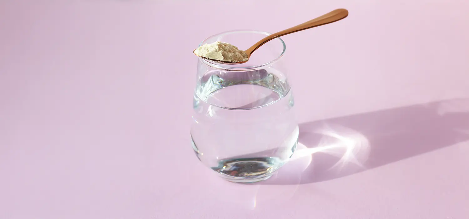 Collageen: wat zegt de wetenschap écht? Glas water met collageenpoeder op roze achtergrond