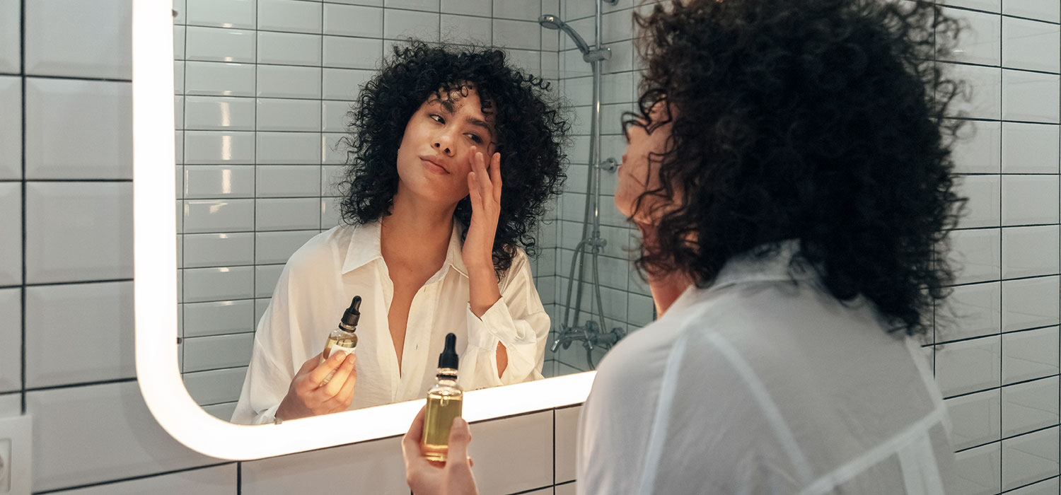 Stralende glans tips voor direct zichtbaar resultat Vrouw brengt serum aan op haar gezicht terwijl ze in de spiegel kijkt