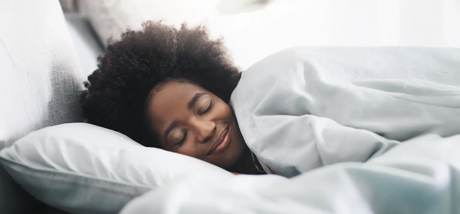 Hoe je weer goed kunt slapen: Antwoorden op veelgestelde vragen Vrouw glimlachend in bed onder het dekbed