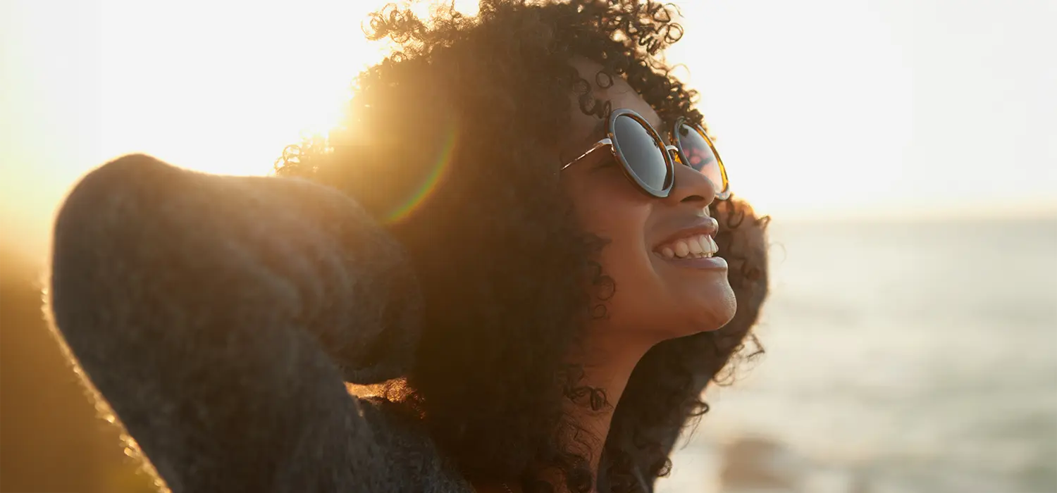 Zie het leven in stijl: optische trends en welzijn voor je ogen Vrouw glimlachend in de zon, zonnebril dragend