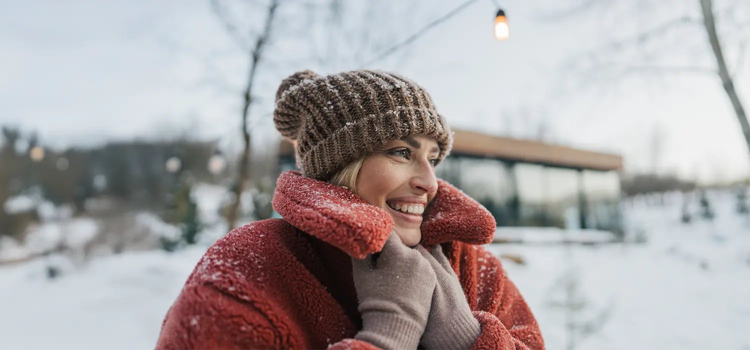 Waarom verdwijnt je glow in de winter? Vrouw met muts en dikke jas buiten in een besneeuwde omgeving