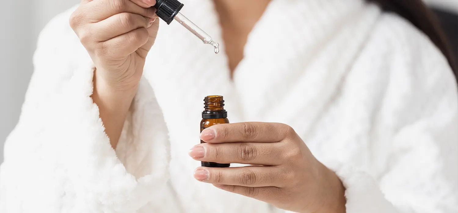 De actieve ingrediënten die je nooit mag combineren — en de duo’s die wél werken Vrouw in badjas met een flesje huidverzorgingsproduct in haar hand